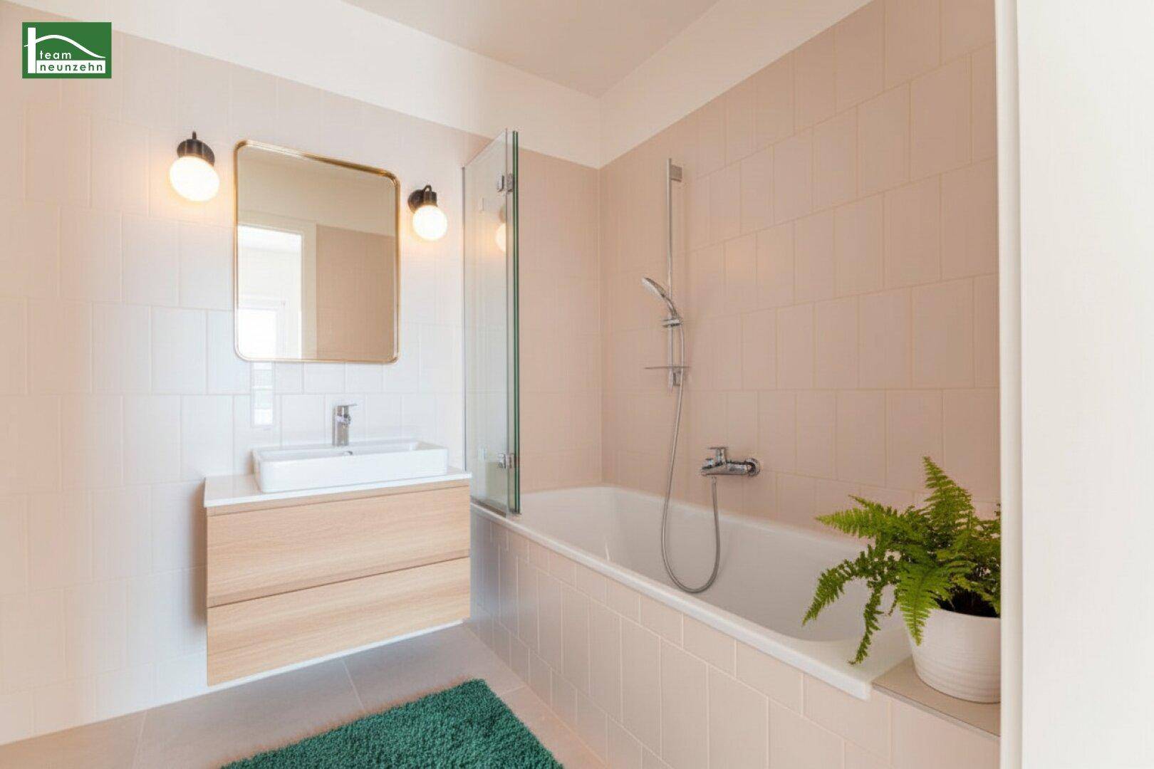 Modernisiertes Badezimmer mit Badewanne, Waschtischunterschrank und Spiegel, in hellrosa Fliesen gehalten.