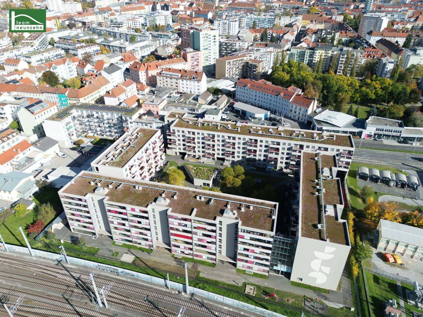 Luftaufnahme eines modernen Wohnkomplexes mit begrünten Dächern und Innenhof in städtischer Umgebung.