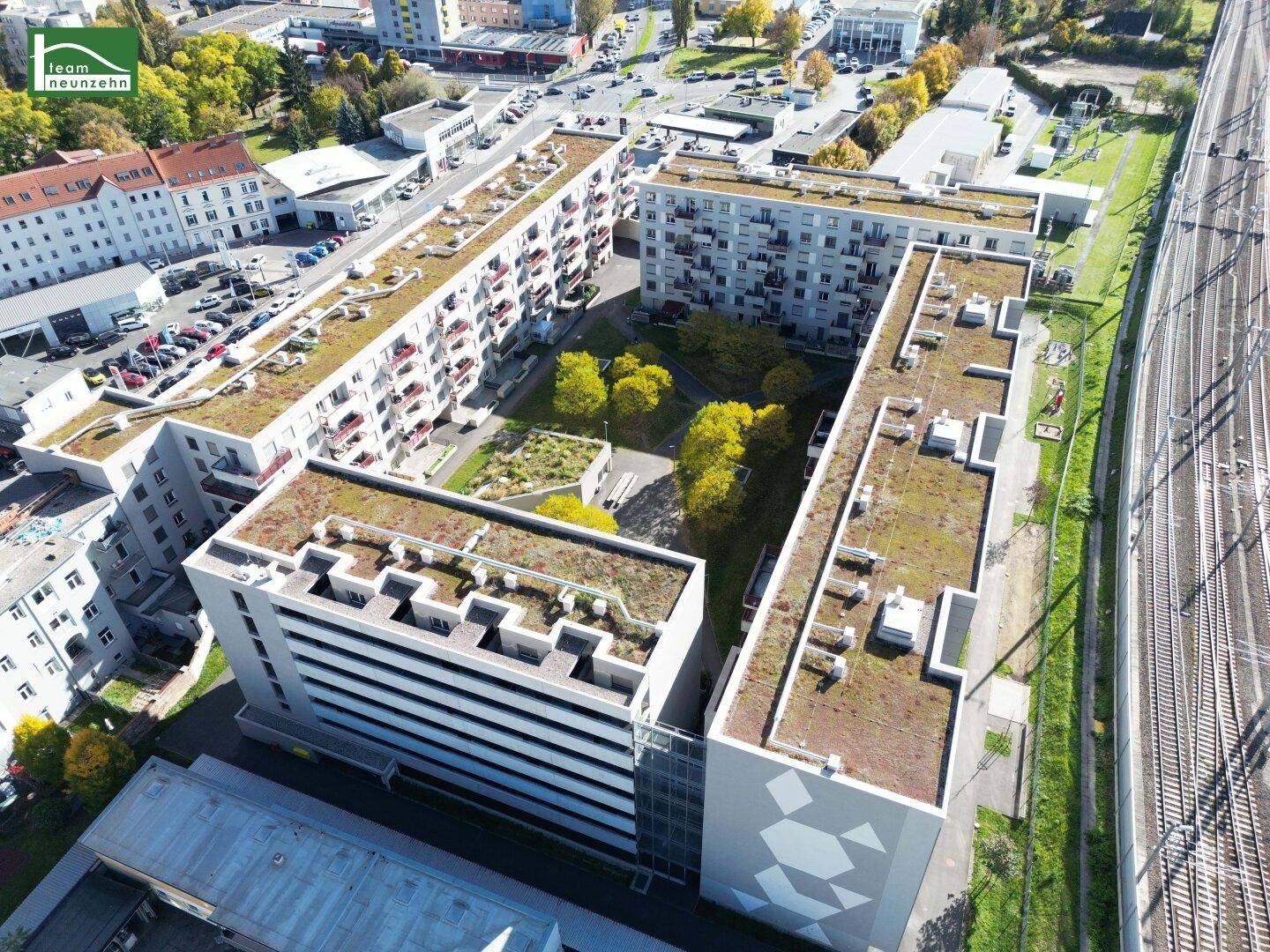 Luftaufnahme eines Wohnkomplexes mit begrüntem Innenhof und angrenzenden Bahngleisen.
