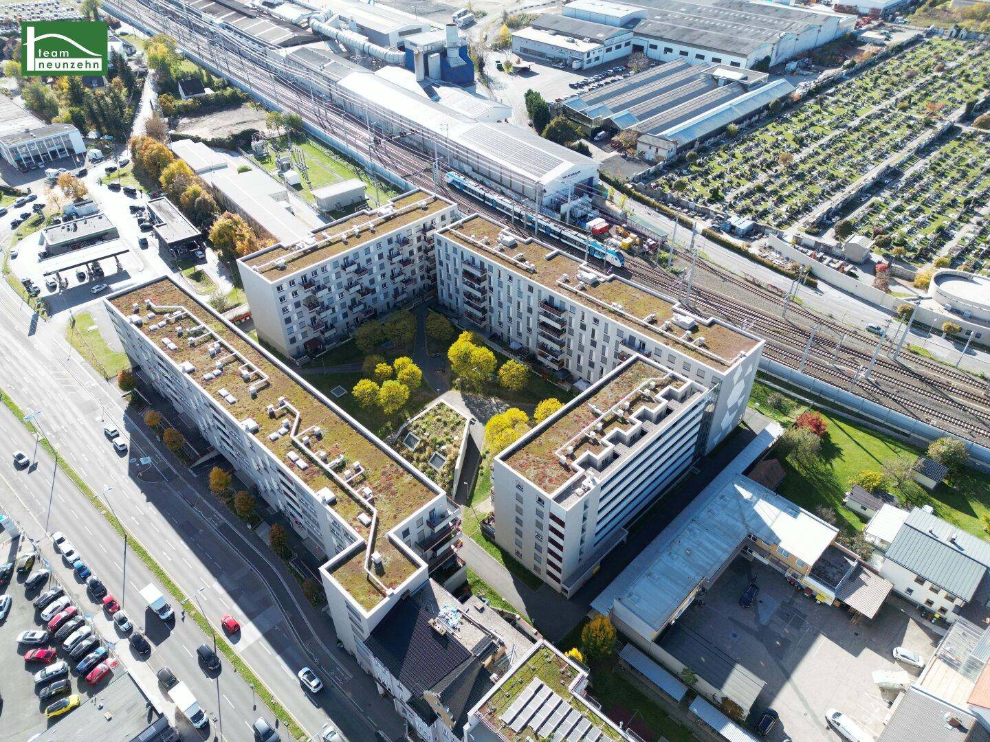 Luftaufnahme eines Wohnkomplexes mit begrünten Dächern und Bahngleisen im Hintergrund.