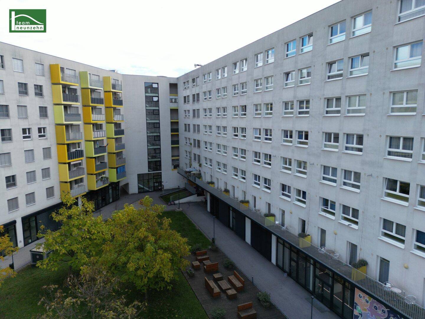 Innenhof eines Wohnkomplexes mit Grünflächen und Sitzgelegenheiten, umgeben von Gebäudefassaden.
