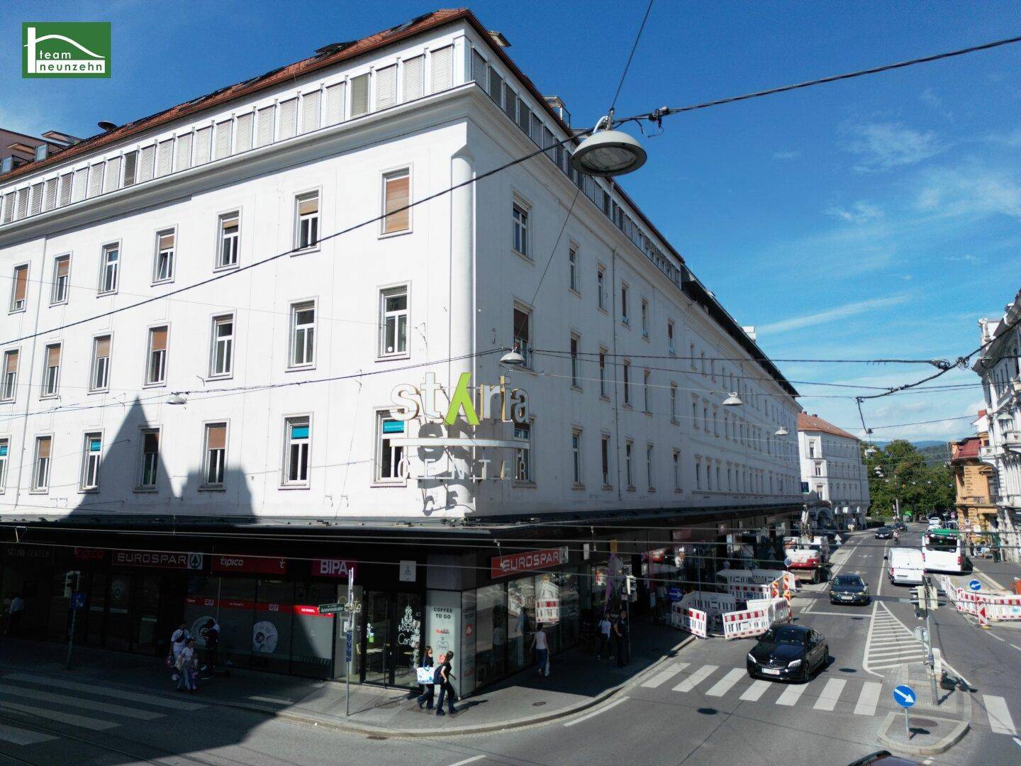 Eckgebäude mit Geschäften im Erdgeschoss an einer belebten Straße in der Stadt.