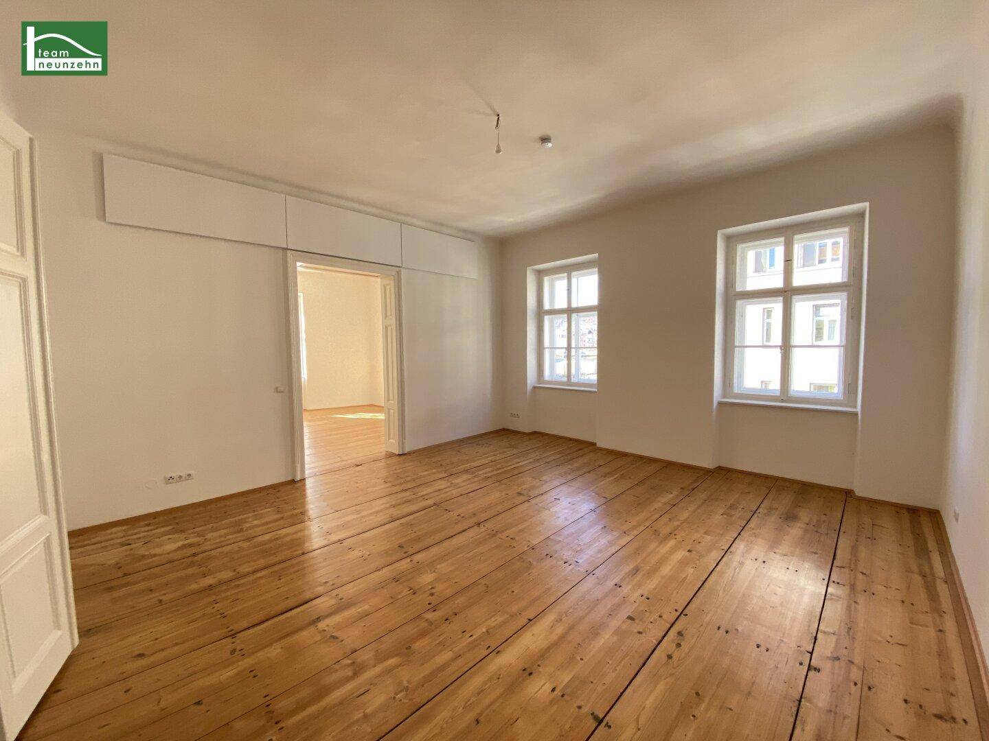 Helles Schlafzimmer mit Holzboden, zwei Fenstern und integrierten Oberschränken über dem Durchgang.