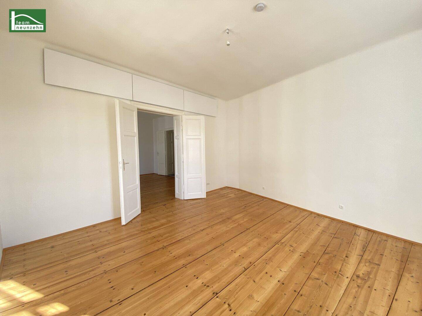 Geräumiges Zimmer mit Holzboden und hohen Decken, mit Oberschränken über dem Türrahmen.