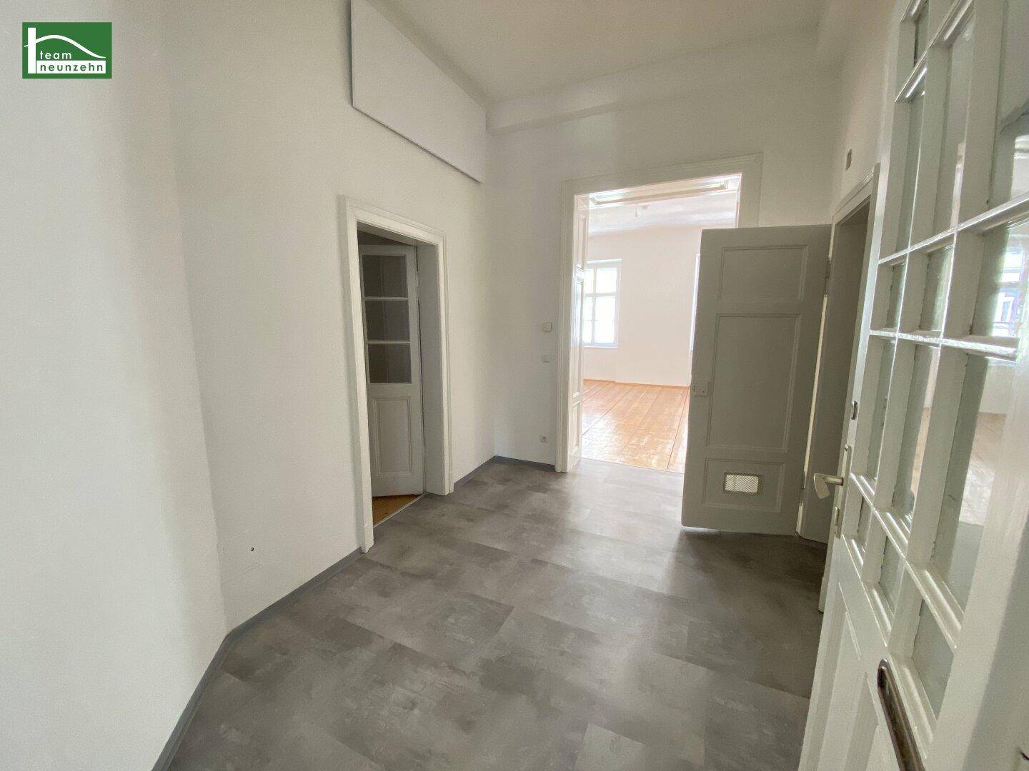 Geräumiger Flur mit grauen Fliesen, der zu verschiedenen Zimmern der Wohnung führt.