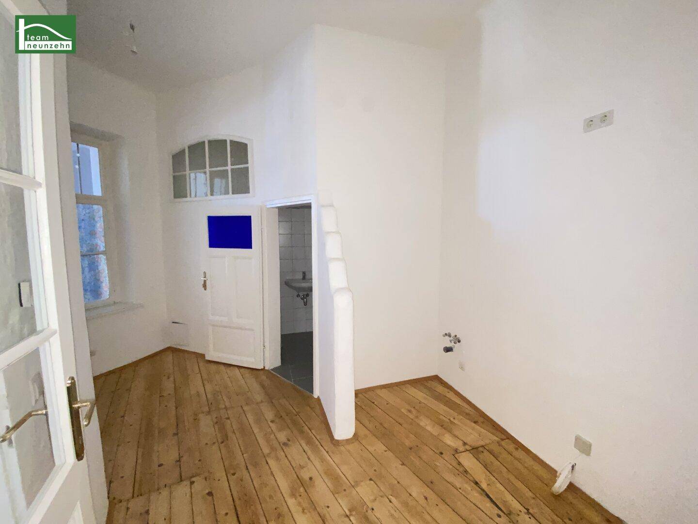 Zimmer mit Holzboden und Zugang zu einem kleinen Badezimmer, mit einem blauen Wandelement.