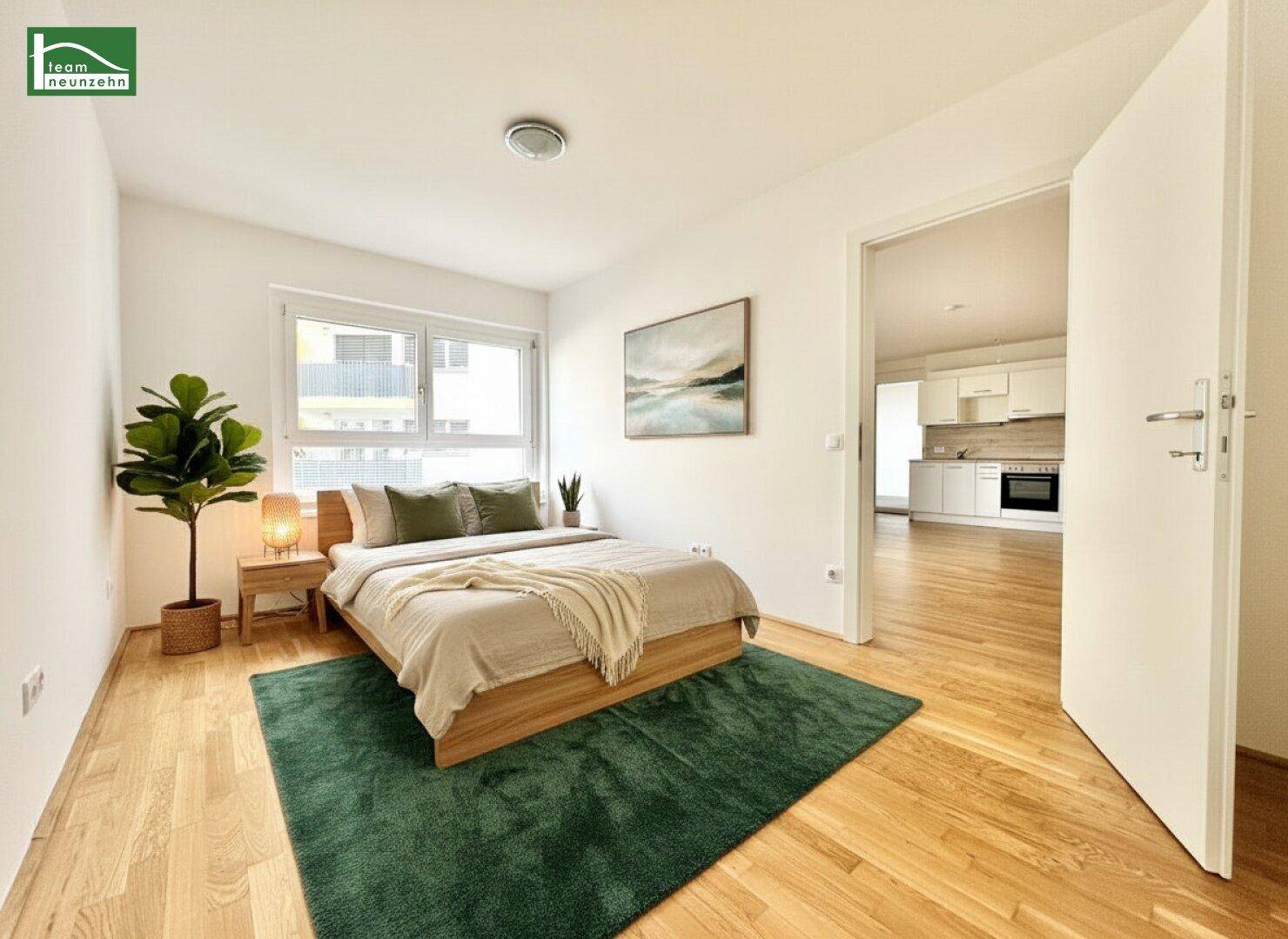 Helles Schlafzimmer mit Holzboden, modernem Bett und Blick in die angrenzende Küche.