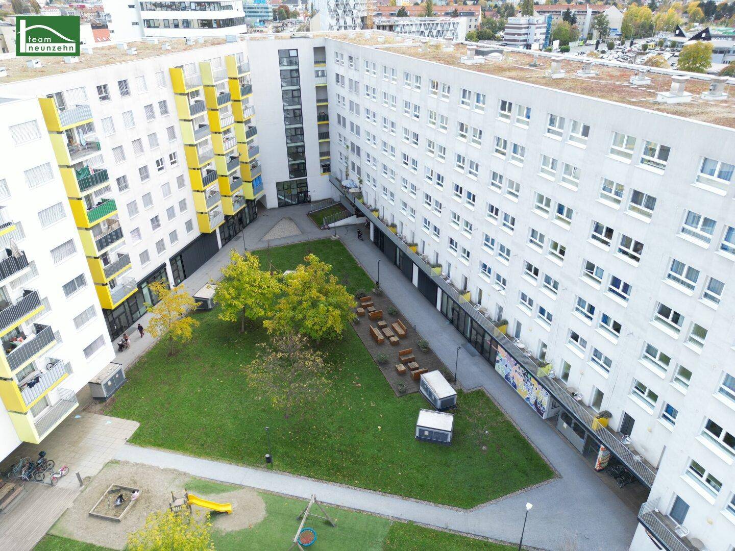 Luftaufnahme eines modernen Wohnkomplexes mit begrüntem Innenhof und Kinderspielplatz.
