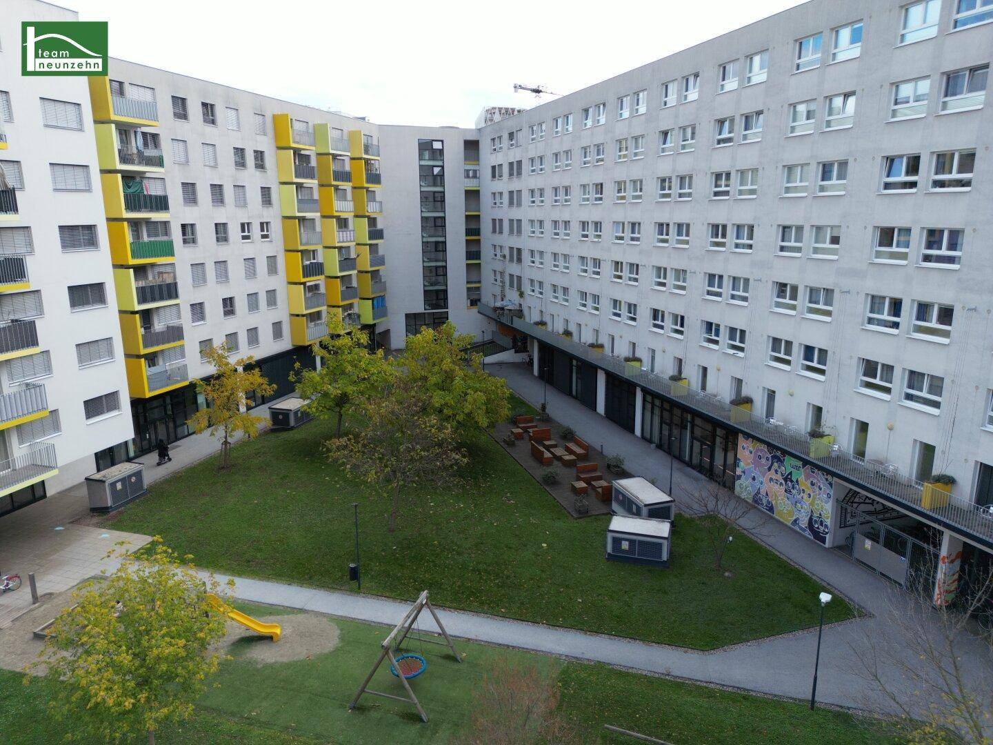 Grüner Innenhof des Wohnkomplexes mit Spielplatz und modernen Fassaden der umliegenden Gebäude.