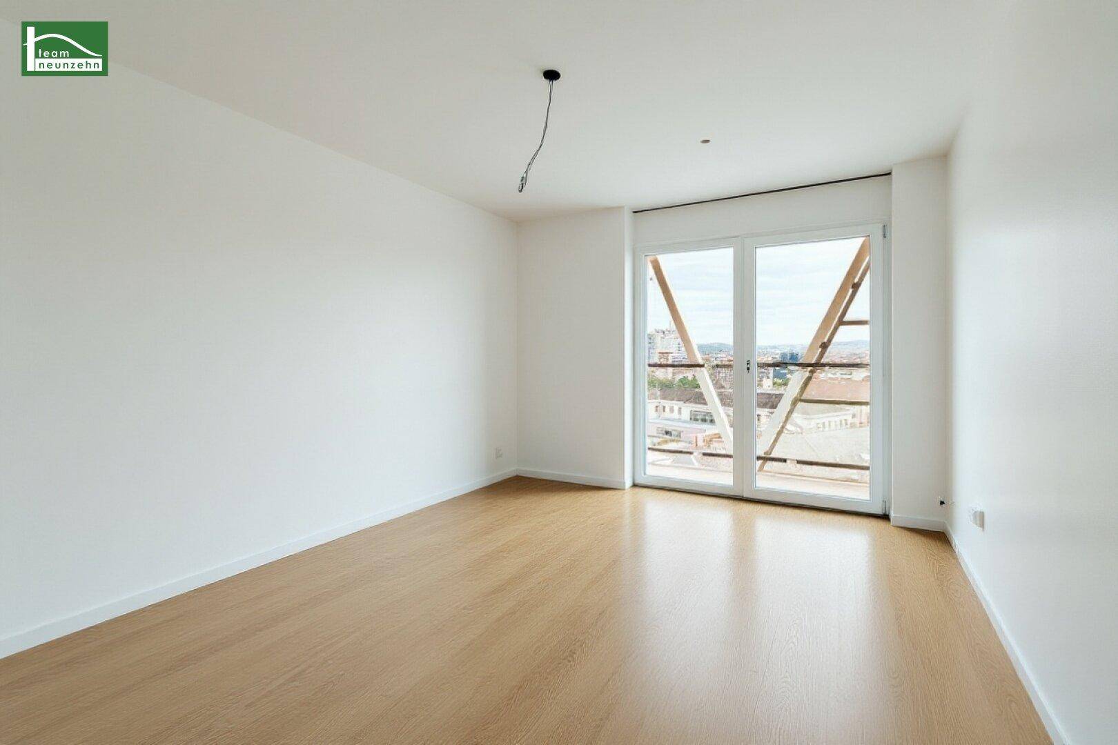 Leeres Schlafzimmer mit Holzboden und großen Fenstern, die viel Tageslicht hereinlassen.