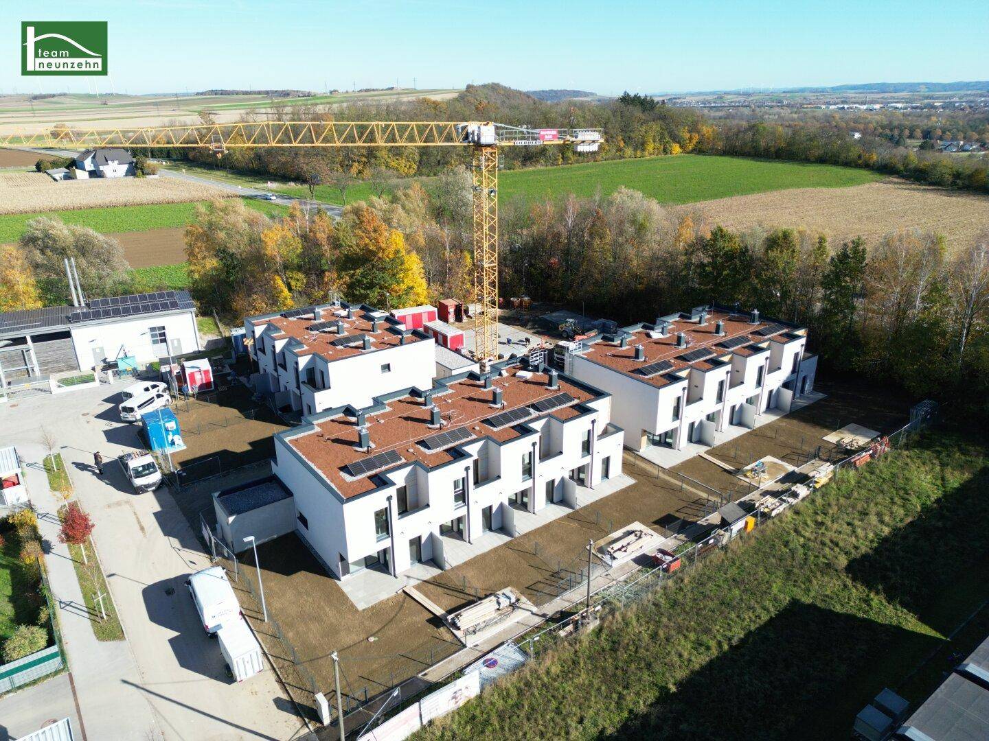 Luftaufnahme der Reihenhausbebauung mit Baukran und umliegender Landschaft im Herbst.