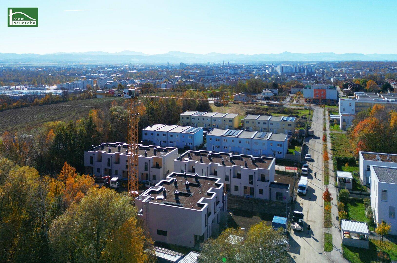 Weitläufige Luftaufnahme der Neubausiedlung mit umliegender Bebauung und Fernblick auf die Stadt.