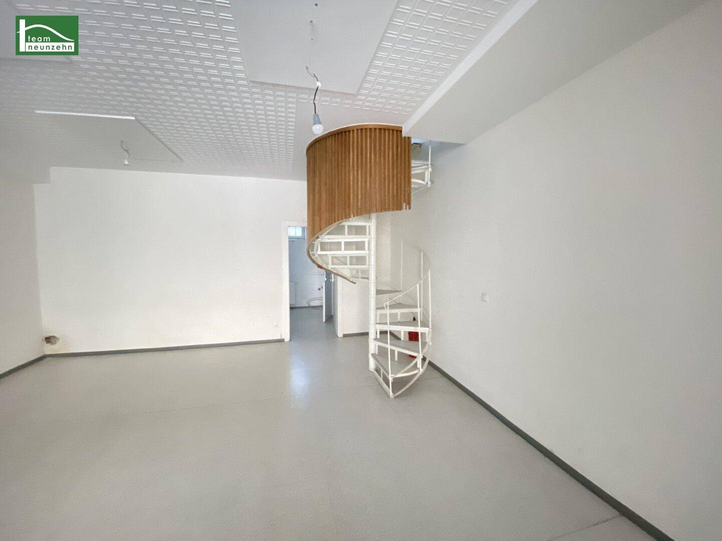 Offener Gewerberaum mit einer markanten weißen Wendeltreppe und Holzverkleidung, die zur oberen Ebene führt.