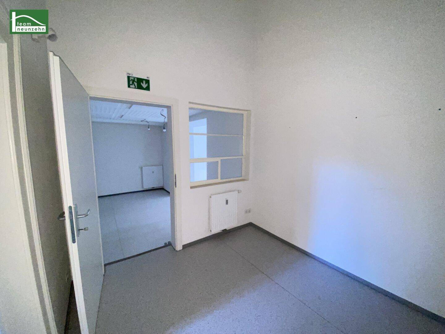 Kleiner, heller Büroraum mit grauem Boden, weiß gestrichenen Wänden und einem Fenster zur Belüftung.