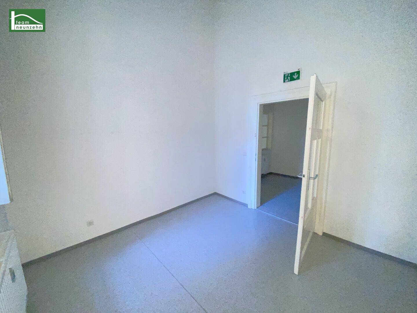 Heller, unmöblierter Raum mit weiß gestrichenen Wänden und einer Tür, die den Zugang zu einem Nebenraum ermöglicht.