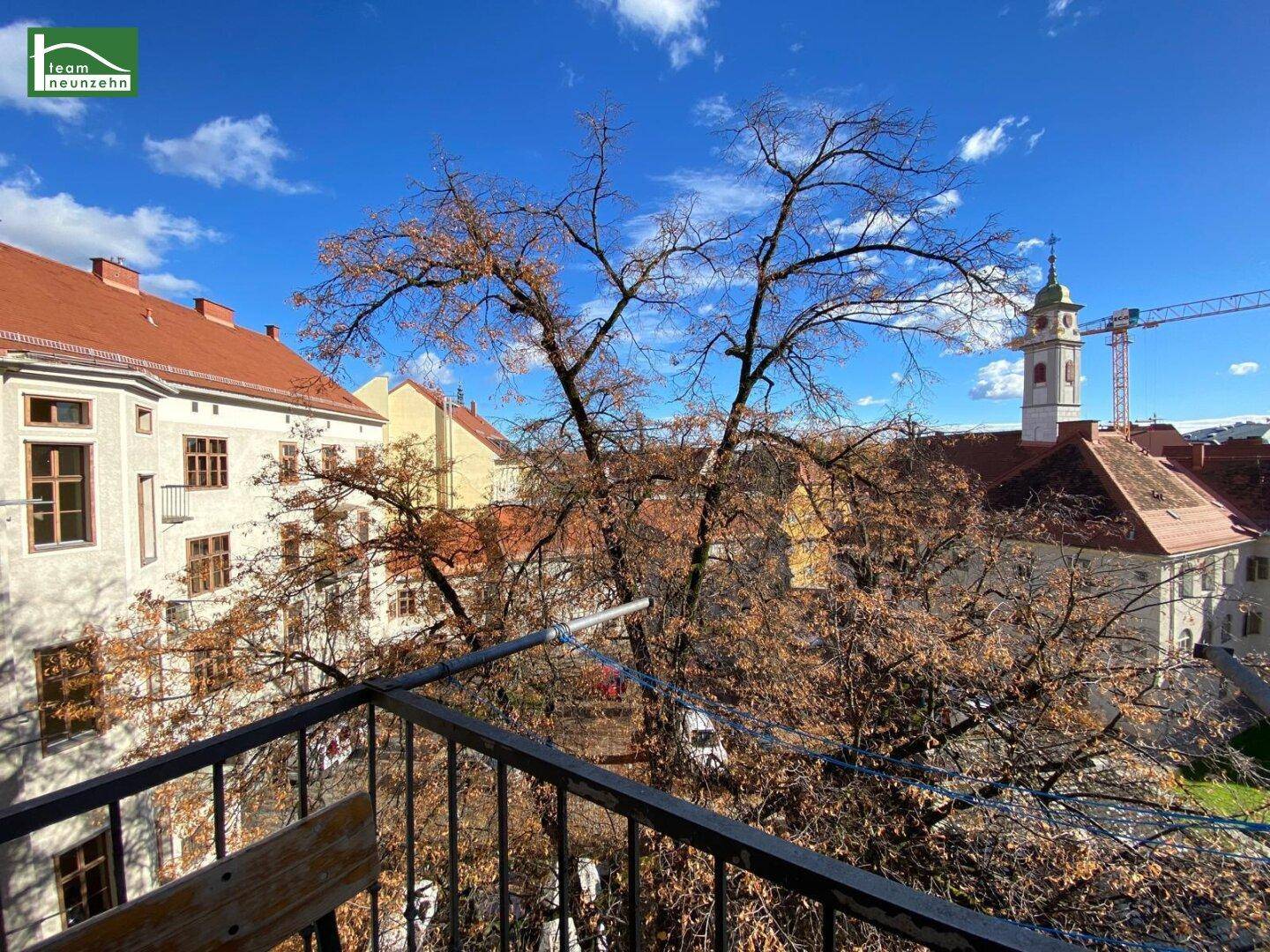 Blick vom kleinen Balkon auf alte Gebäude und herbstliche Bäume in der Umgebung.
