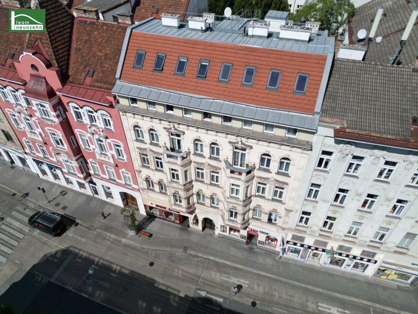 Luftaufnahme der historischen Gebäudefassade mit rotem Mansarddach und umliegender Straße.