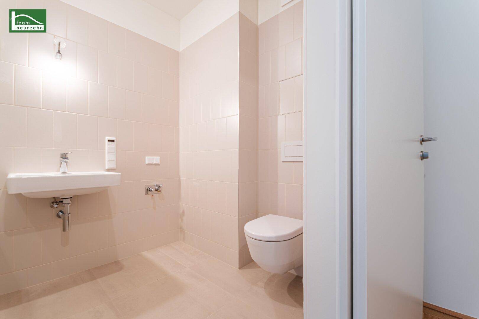 Modernes WC mit wandhängender Toilette und kleinem Waschbecken, hell gefliest.
