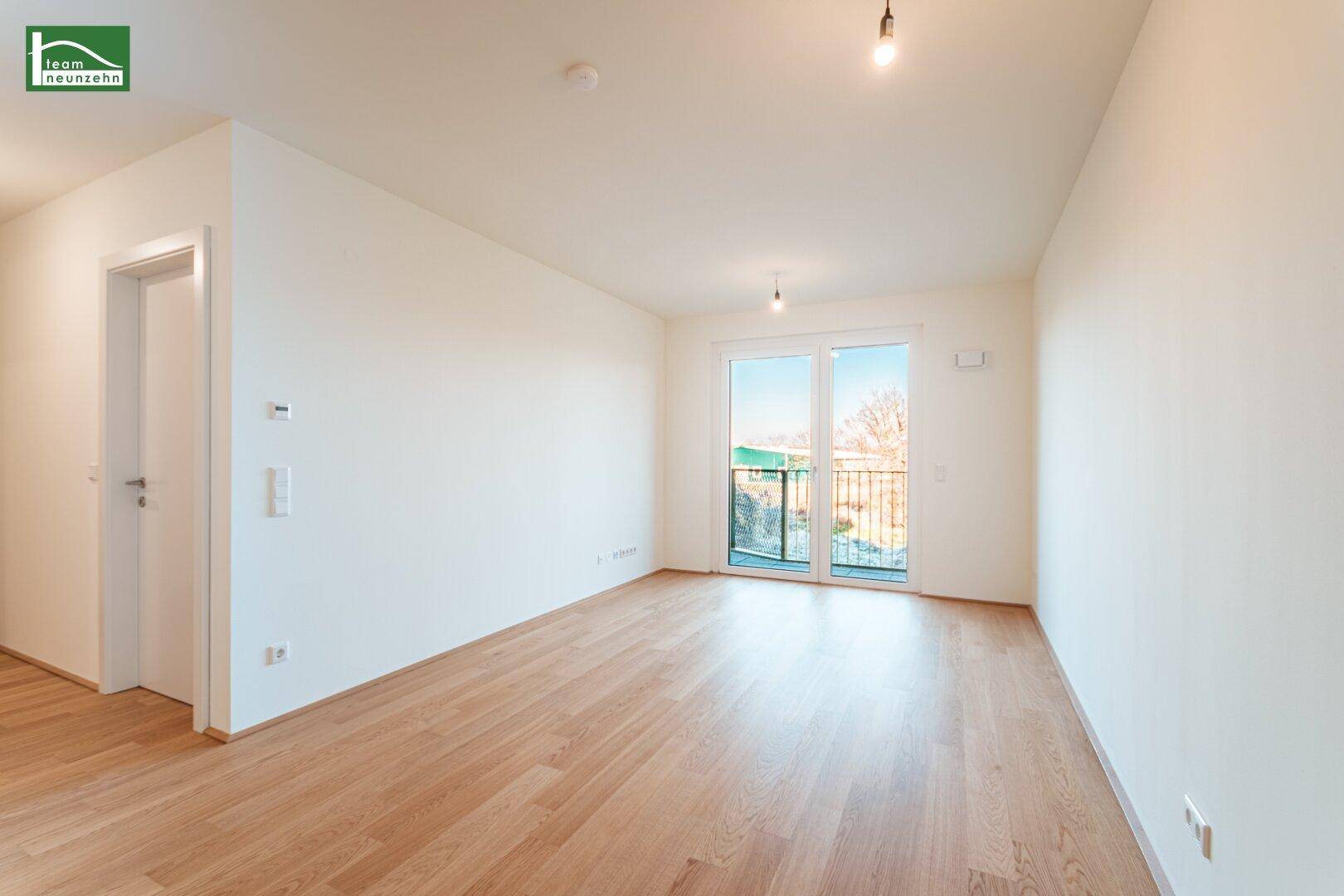 Heller, unmöblierter Wohnraum mit Holzboden und Zugang zu einem Balkon.