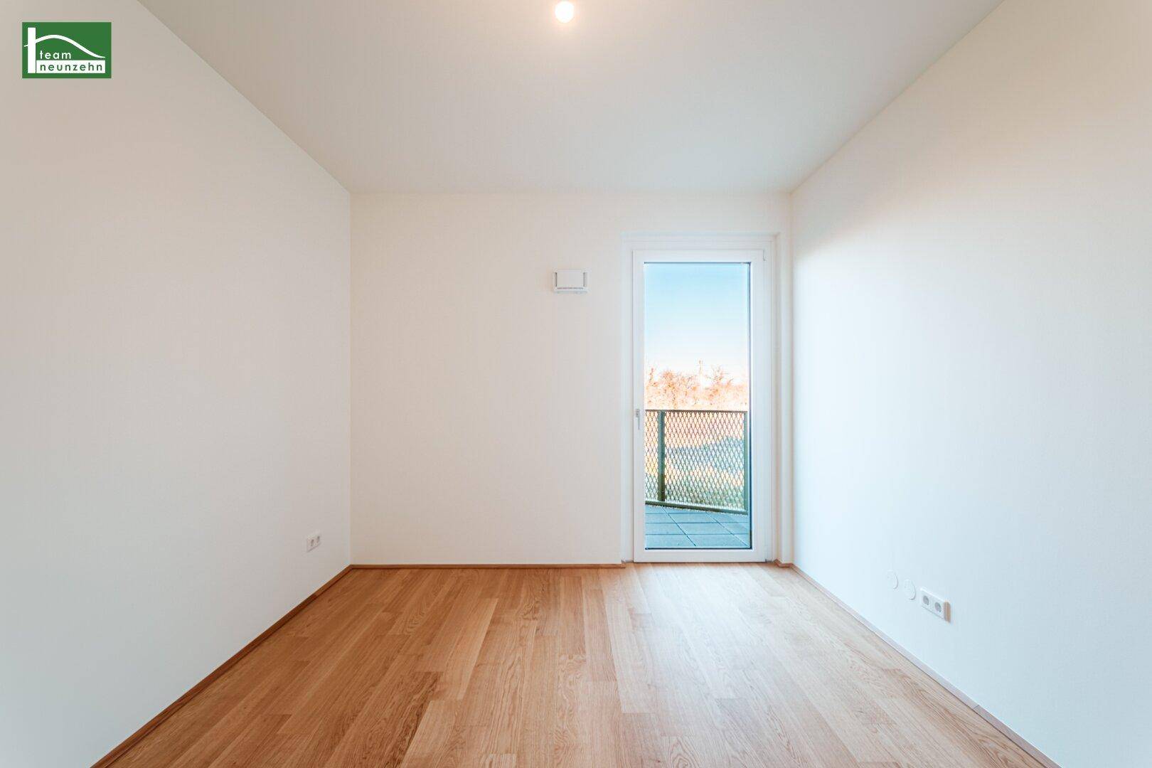 Leeres Schlafzimmer mit Parkettboden, hellen Wänden und direktem Zugang zum Balkon.