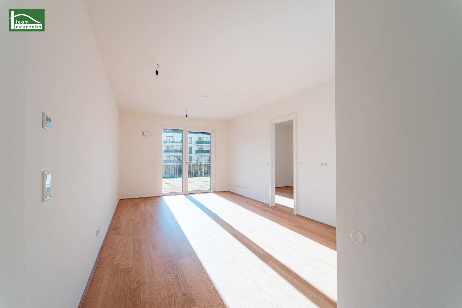 Lichtdurchfluteter Raum mit Schiebetüren zum Balkon und hellem Holzboden.
