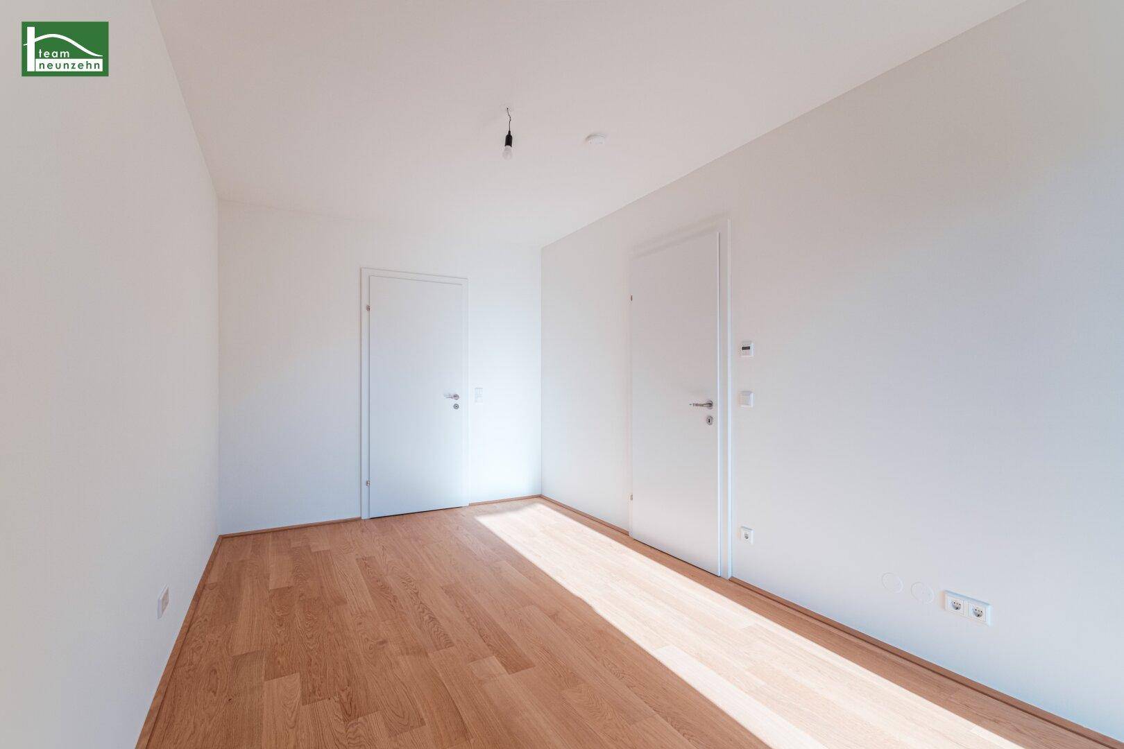 Leeres Zimmer mit Holzboden und zwei Türen, bietet vielseitige Nutzungsmöglichkeiten.