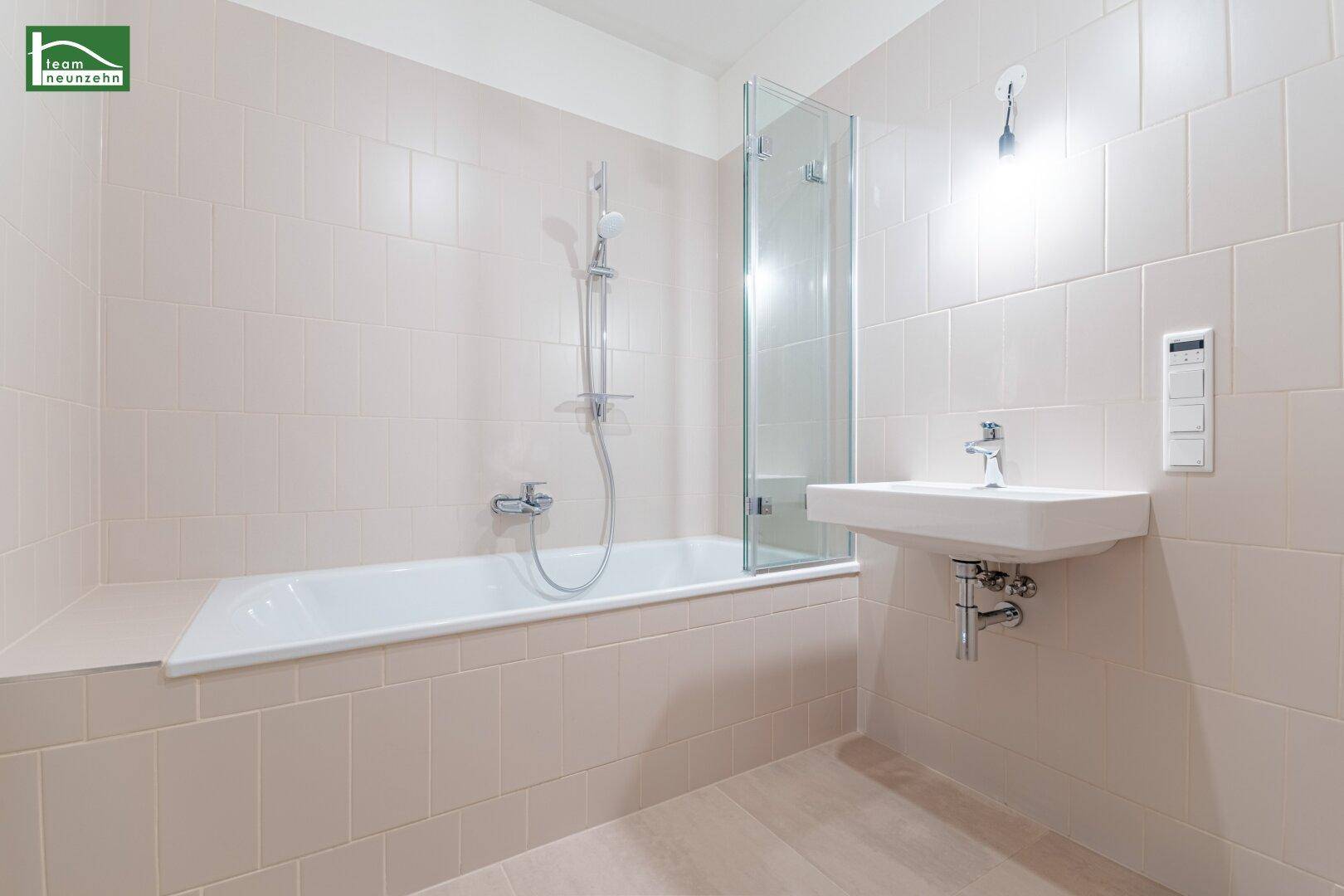 Modernes Badezimmer mit Badewanne, Duschwand und hellem Fliesenboden.