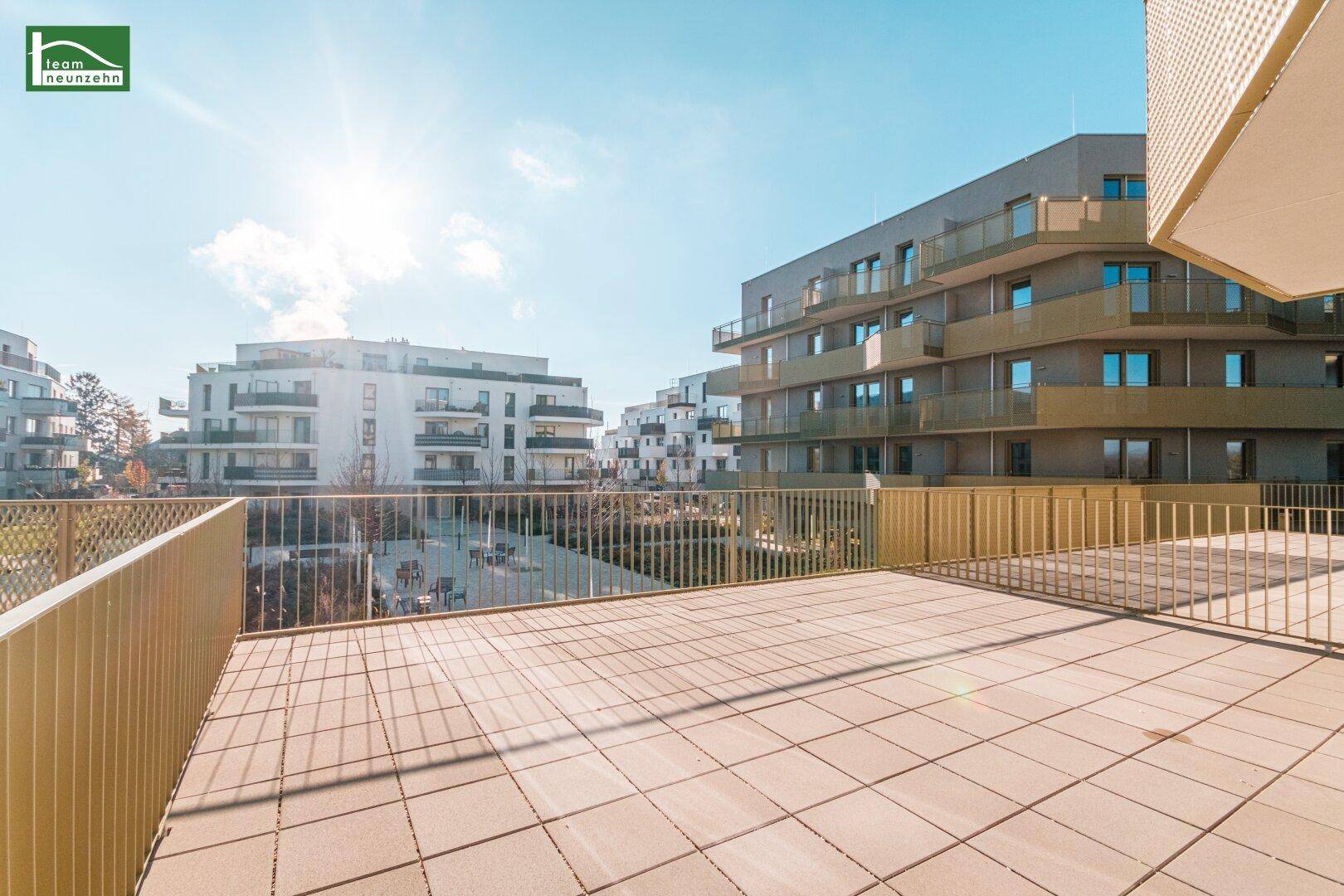 Große, sonnige Terrasse mit Fliesenboden und Blick auf moderne Wohngebäude.