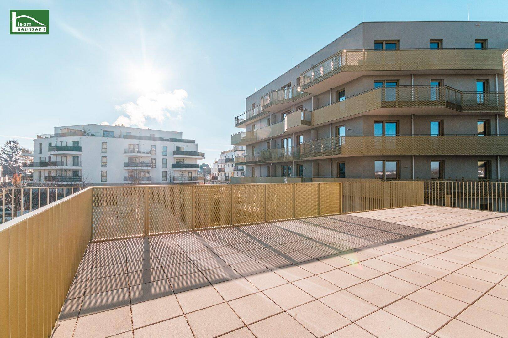 Große, sonnige Terrasse mit modernen Fliesen und Blick auf umliegende Wohngebäude.
