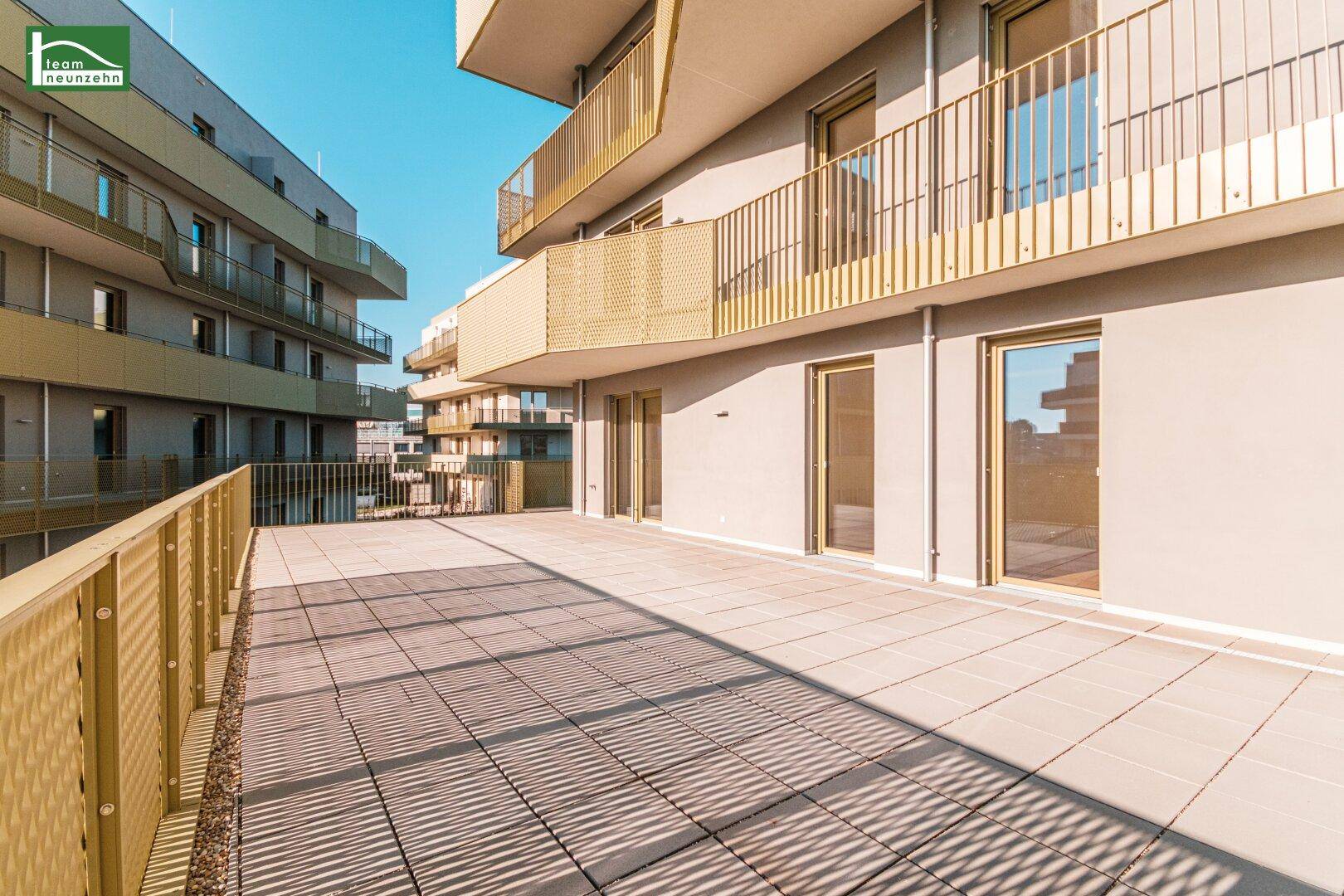 Weitläufige Terrasse mit modernen Fliesen und Blick auf die Fassade des Neubaus.