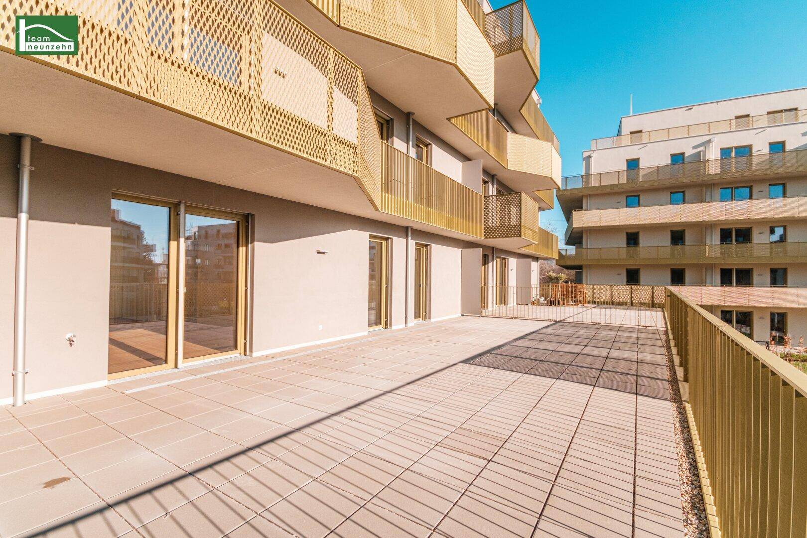 Große, sonnige Terrasse mit Fliesenboden und Blick auf die moderne Architektur der Wohnanlage.