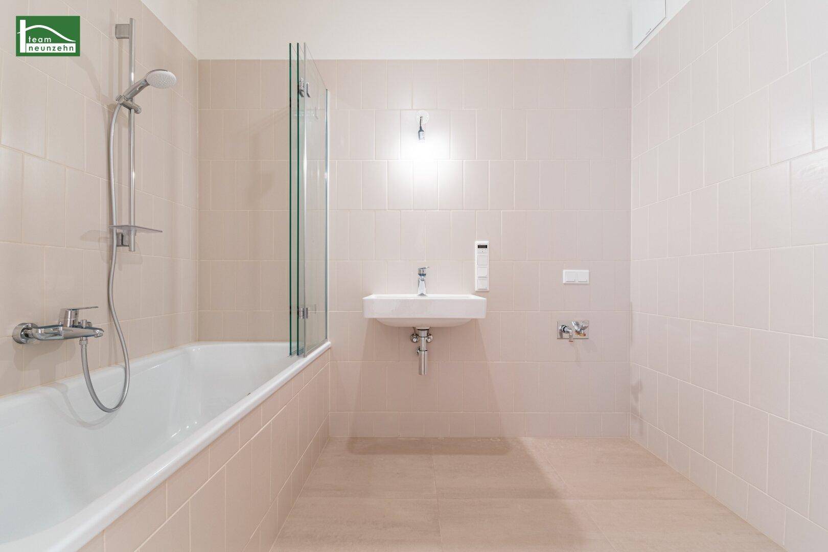 Modernes Badezimmer mit Badewanne, Duschvorrichtung und hellen Fliesen.