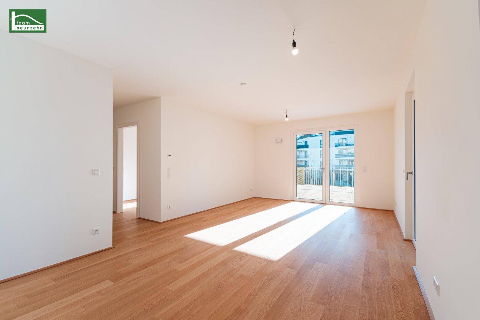 Geräumiges, leeres Wohnzimmer mit Holzboden und Zugang zu einem Balkon oder einer Terrasse.
