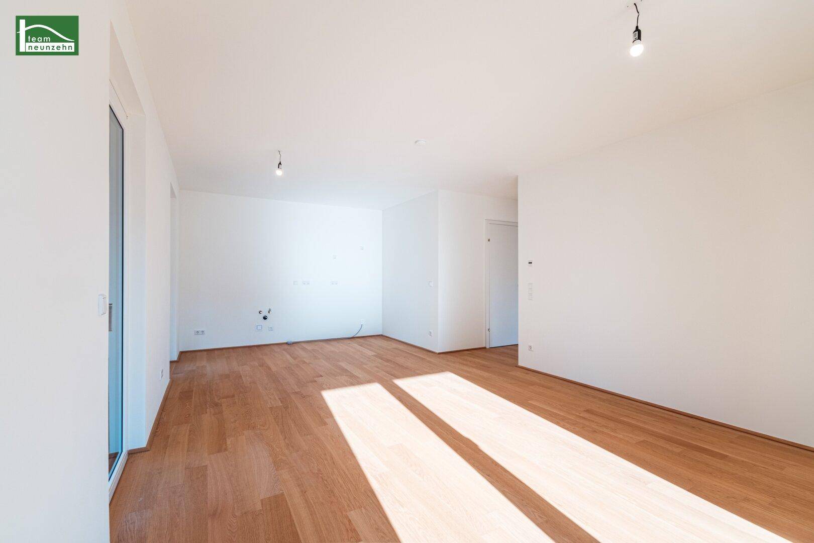 Geräumiges, leeres Zimmer mit Holzboden und viel Tageslicht, ideal als Wohnbereich.