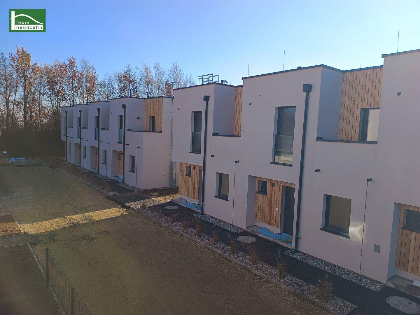 Reihenhäuser in moderner Architektur mit flachen Dächern und Holzdetails, umgeben von Natur.