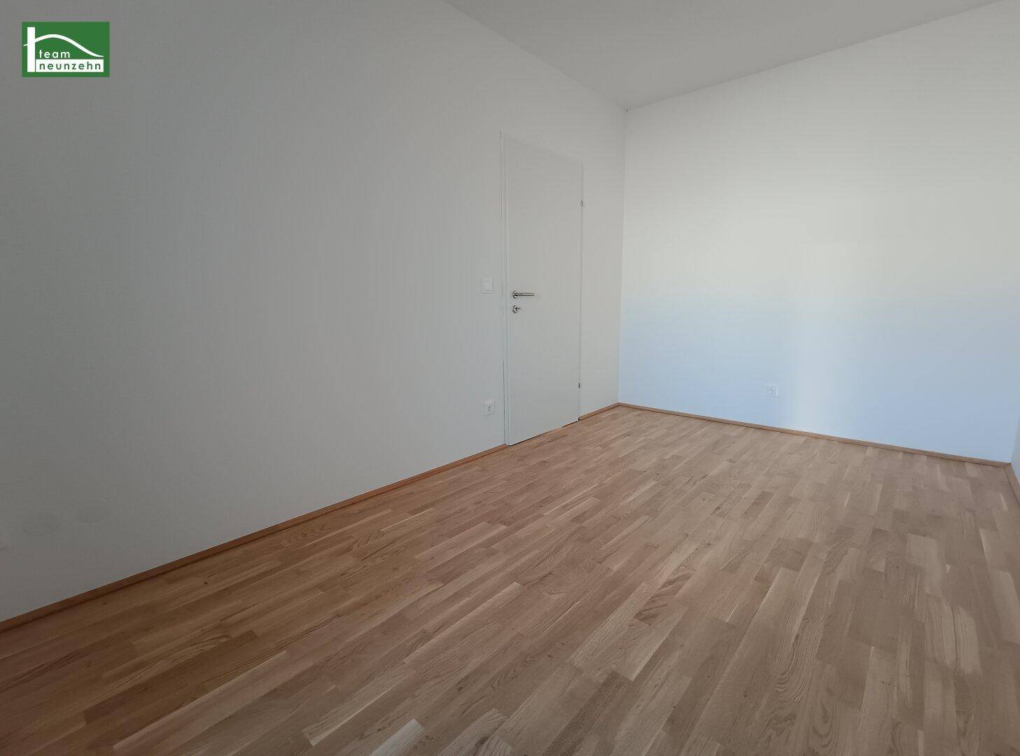 Leeres Zimmer mit Holzboden und weiß gestrichenen Wänden, bereit zur individuellen Gestaltung.