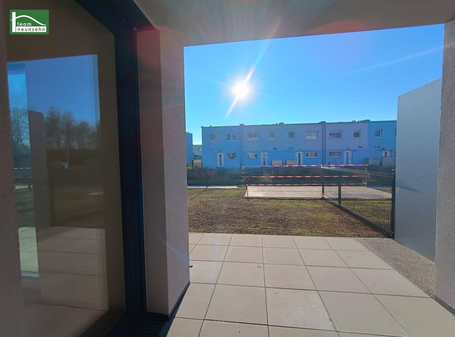 Sonniger Terrassenbereich mit Fliesenboden und Blick auf die gegenüberliegenden Gebäude.