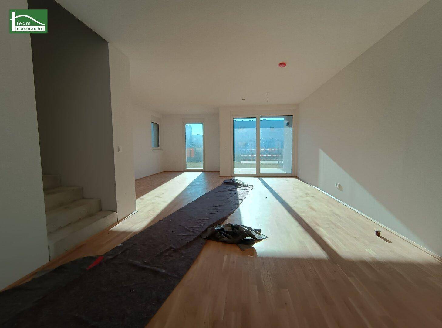 Lichtdurchfluteter Wohnbereich mit Holzboden und Treppenzugang, bereit für die Einrichtung.