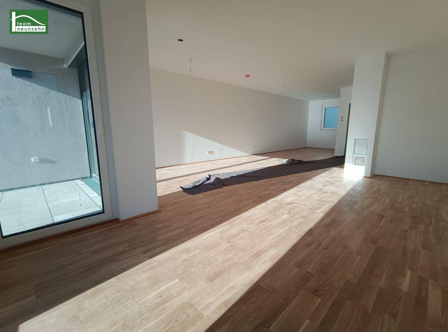 Heller, leerer Wohnbereich mit Holzboden und Zugang zu einem gefliesten Außenbereich.