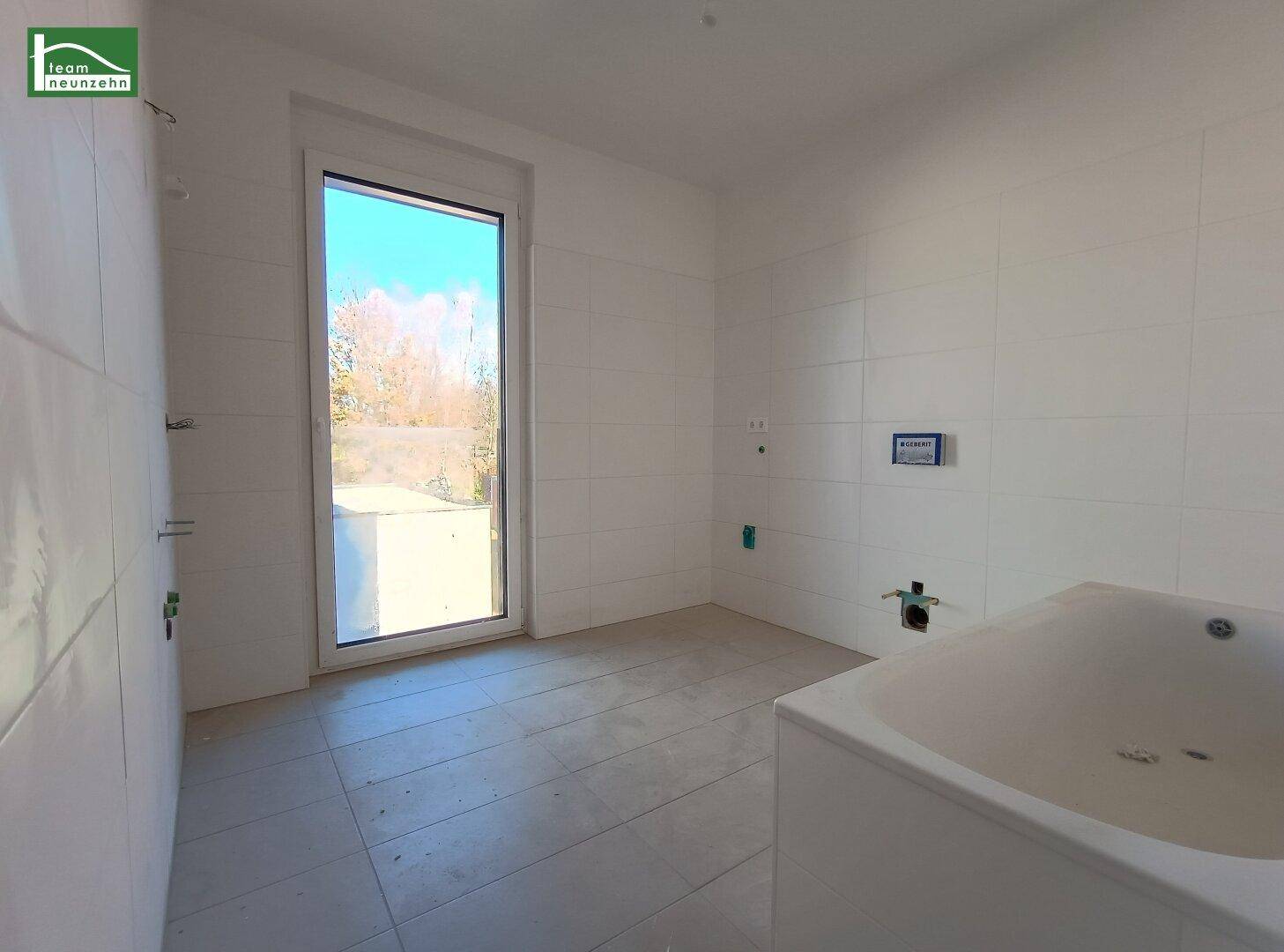 Unfertiges Badezimmer mit weißen Fliesen, Badewanne und Fenster, bereit für den Ausbau.