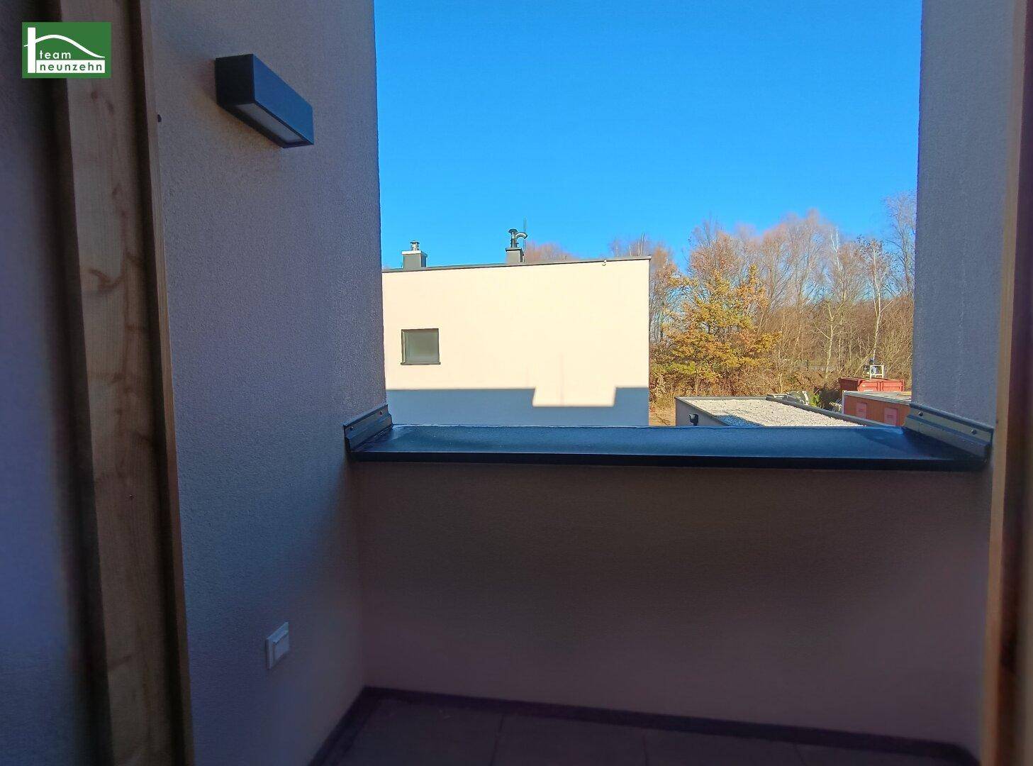 Kleiner Balkon mit Fliesenboden und Blick auf die Umgebung unter blauem Himmel.