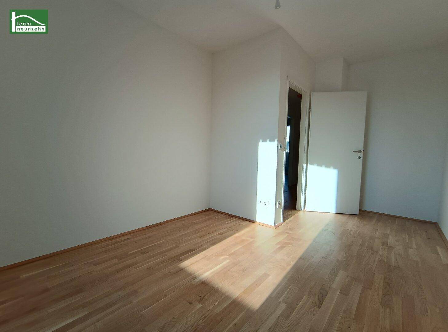 Leeres Zimmer mit Holzboden und weiß gestrichenen Wänden, bereit für die individuelle Einrichtung.