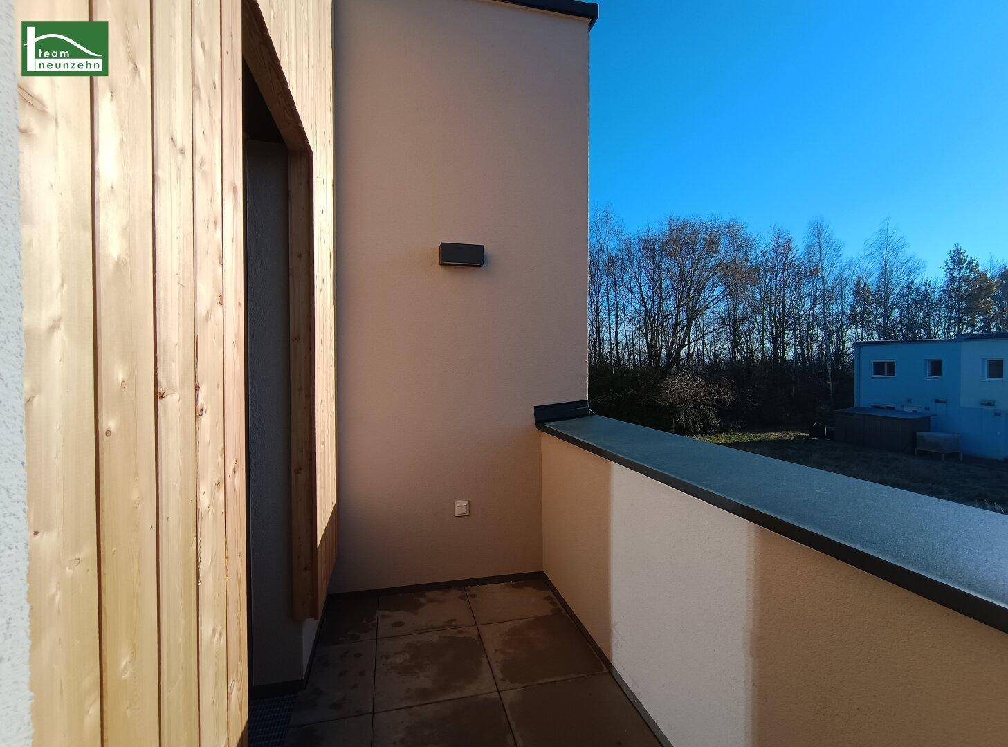 Schmaler Balkon mit Fliesenboden und Holzverkleidung an der Fassade, sonniger Ausblick.