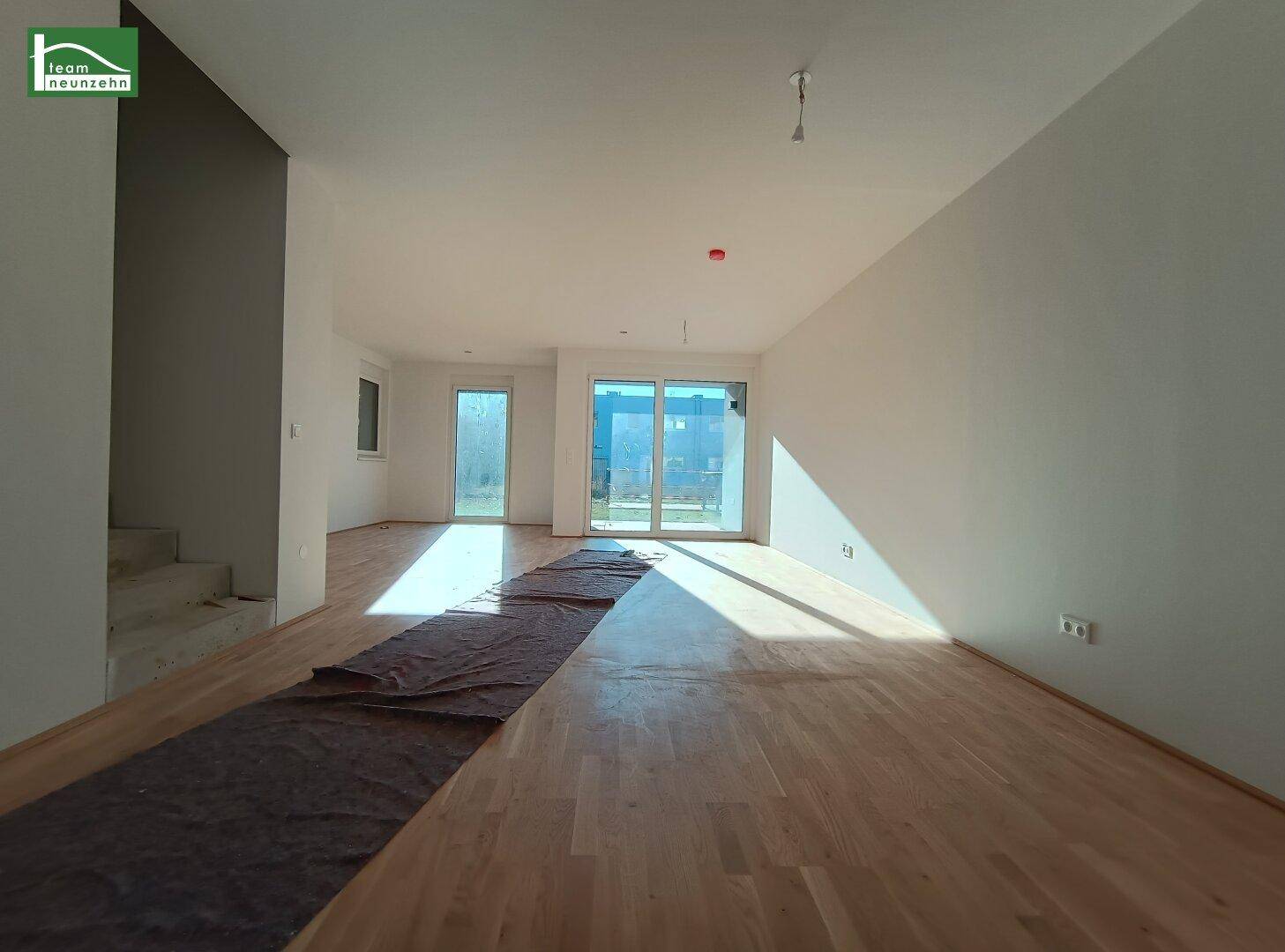 Offener Wohnbereich mit Parkettboden und breiten Fensterfronten, die den Raum erhellen.