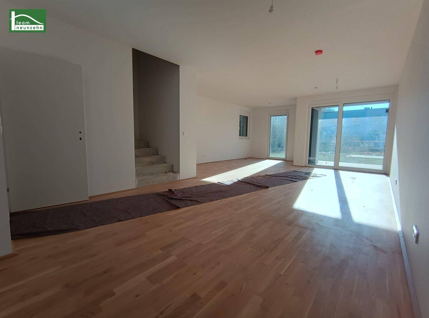 Heller Wohnbereich mit Treppenzugang und großen Fenstern, die viel Licht hereinlassen.