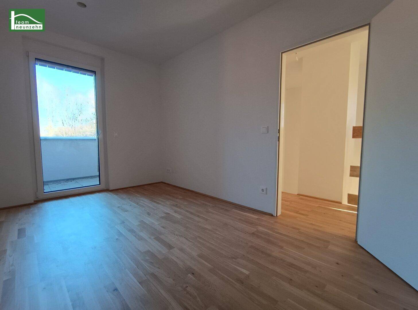 Heller Wohnbereich mit Parkettboden und Zugang zu einem Balkon sowie einem weiteren Raum.