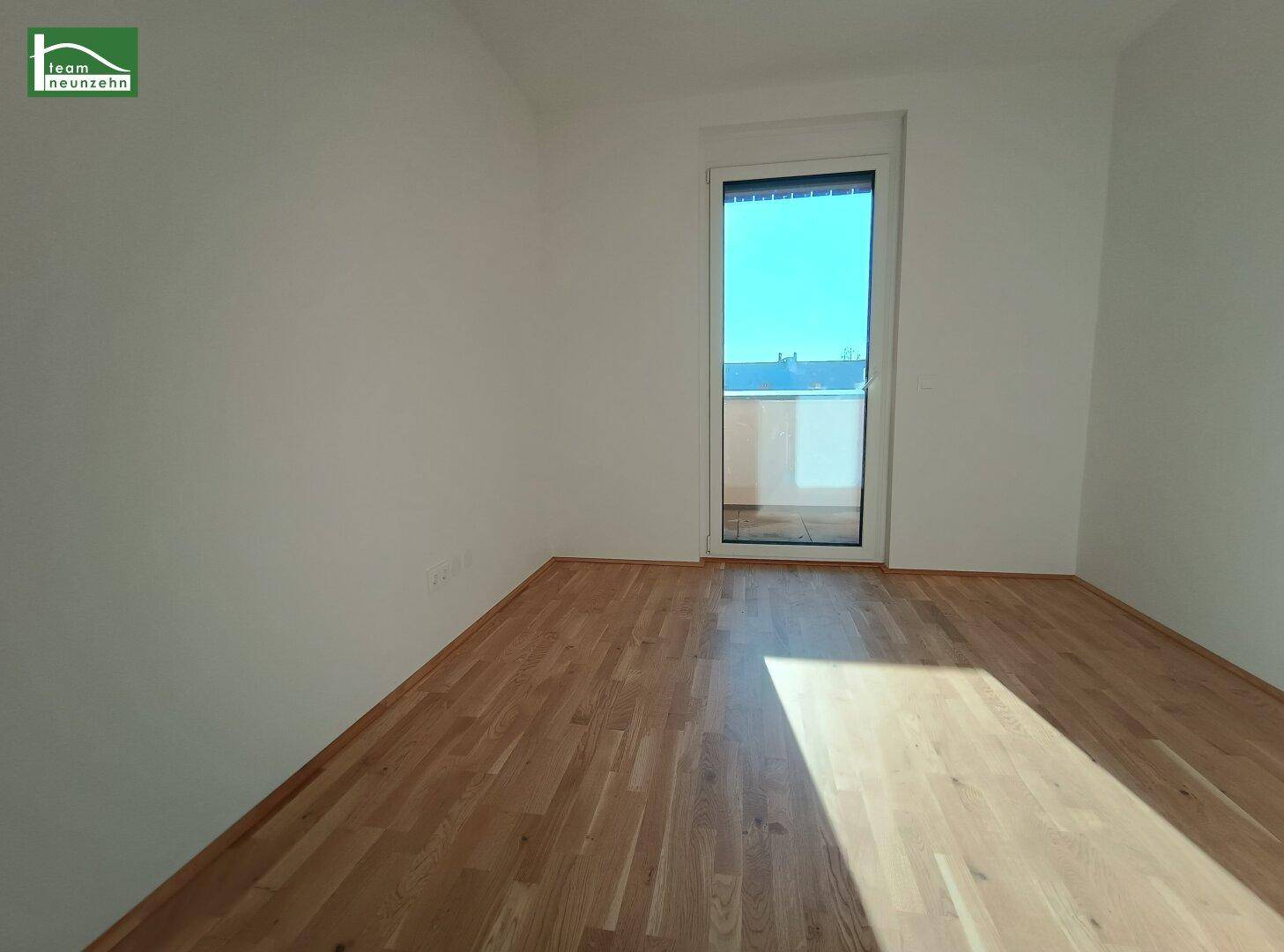 Helles Zimmer mit Parkettboden und Zugang zu einem Außenbereich.