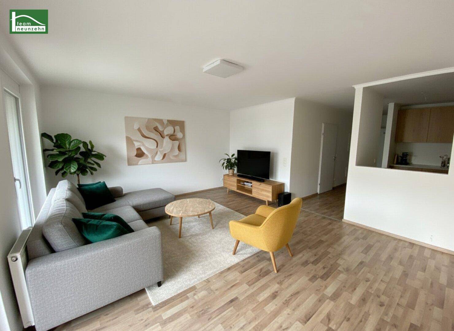 Modern eingerichteter Wohnbereich mit Laminatboden, bequemer Couch und Blick in die halboffene Küche.