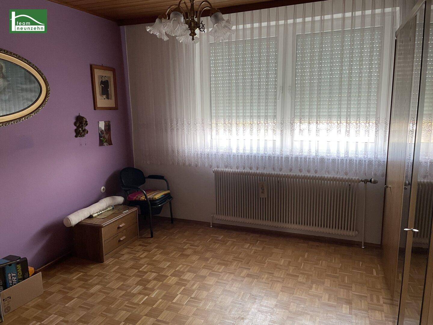 Schlafzimmer mit lila Wänden, Parkettboden und großem Fenster.