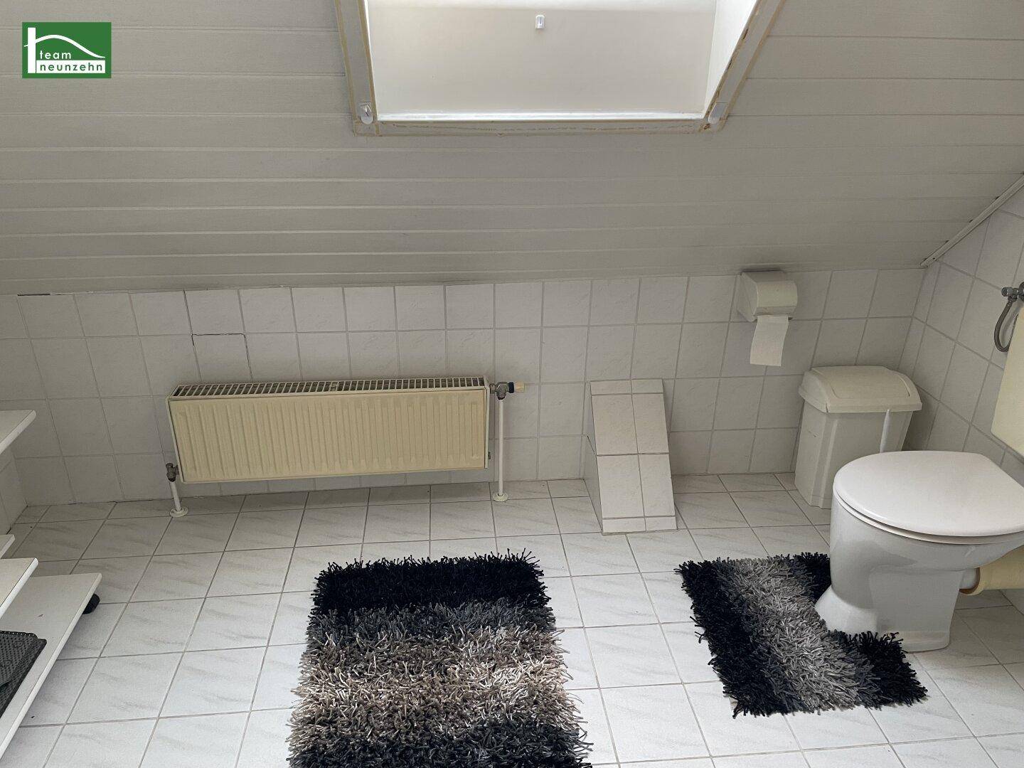 Dachgeschoss-Badezimmer mit Fliesenboden, Toilette, Heizkörper und Dachfenster.